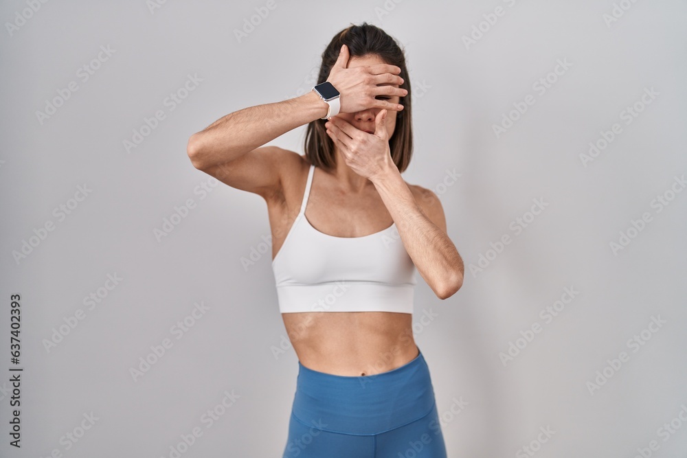 Hispanic woman wearing sportswear over isolated background covering eyes and mouth with hands, surprised and shocked. hiding emotion