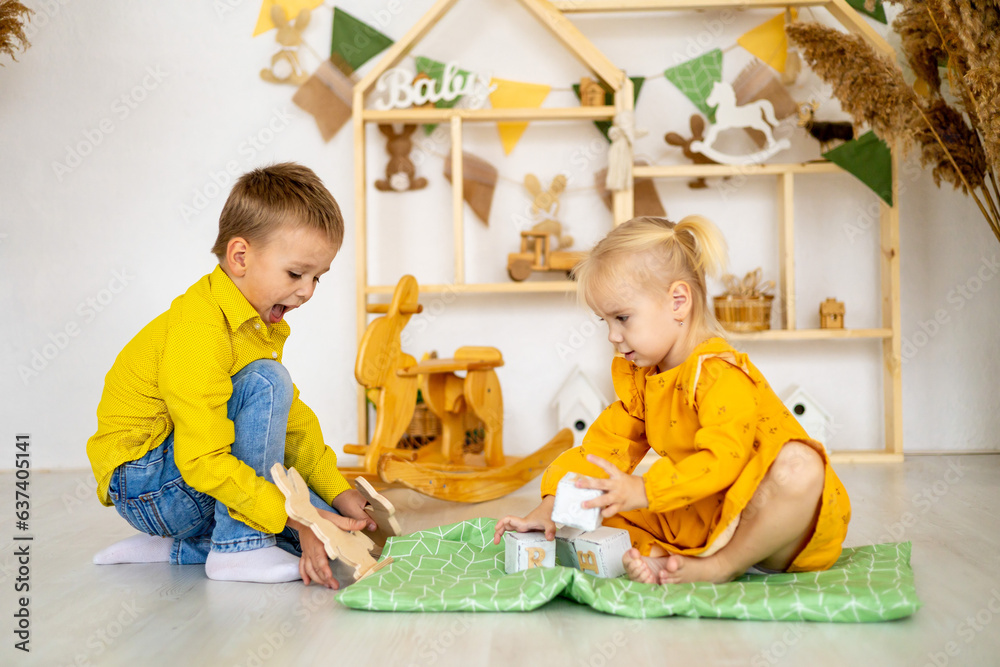 Obraz premium little children girl with boy brace with sister play at home with wooden toys, stands a pyramid or a tower and smiles, happy childhood