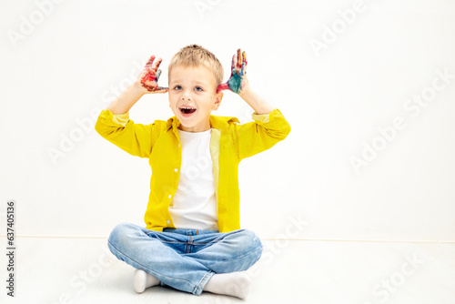 a little boy child with painted hands stained in paint in yellow clothes on a white isolated background was drawing