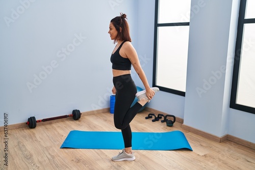 Young beautiful hispanic woman smiling confident stretching leg at sport center
