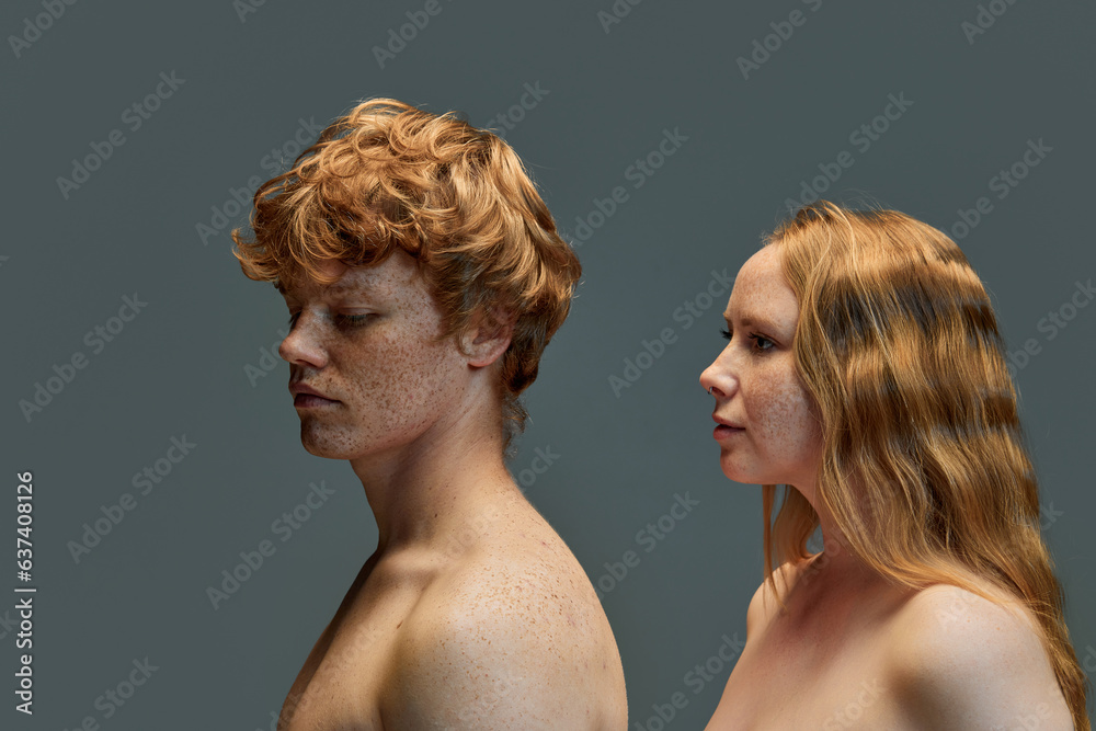 Beautiful red hair couple on grey background, fashion. Beautiful woman with bare shoulders looking at back of guy. Beautiful red hair couple on grey background, fashion. Beautiful woman with bare shoulders looking at back of guy.