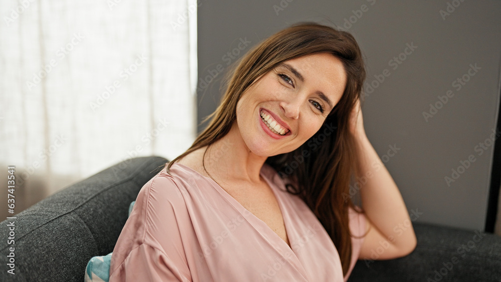 Young beautiful hispanic woman smiling confident sitting on sofa combing hair with hand at home