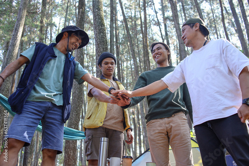Low angle of group of Asian male hiker tourists stacking hands in campsite while hiking in countryside