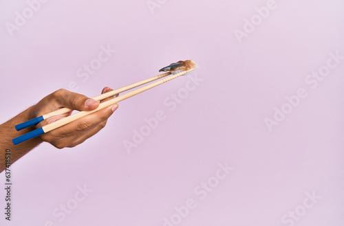  Hand of man holding eel nigiri with chopsticks over isolated pink background