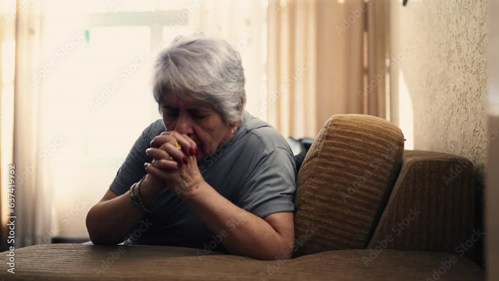 Authentic Elderly Caucasian Female Engaged in Prayer at Home, Senior Individual with Clenched Hands Sitting on Sofa, Epitome of Devotion and Faith