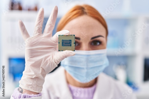 Young caucasian woman scientist wearing medical mask holding cpu processor chip at laboratory