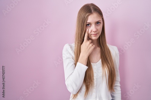 Young caucasian woman standing over pink background pointing to the eye watching you gesture, suspicious expression
