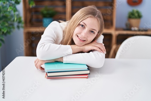 Young caucasian woman smiling confident leaning on books at home