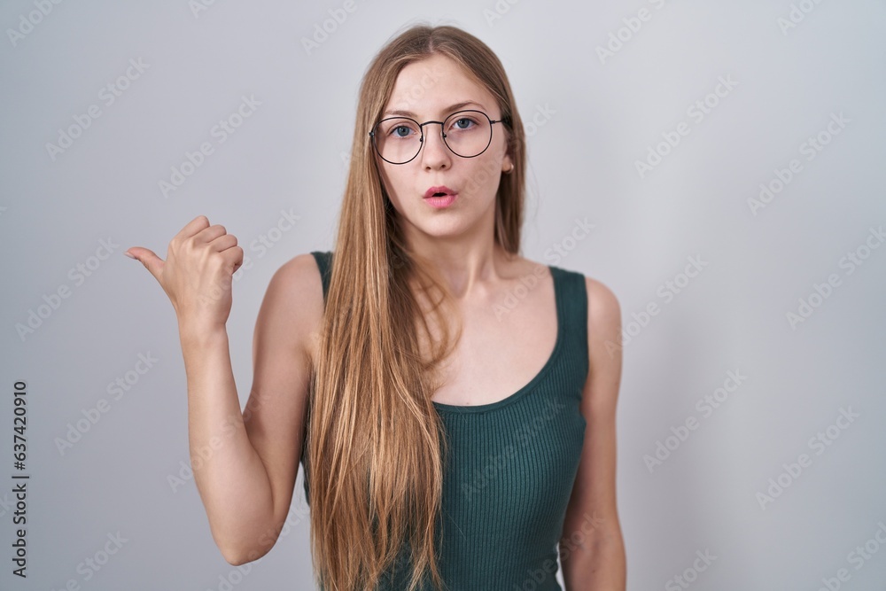 Young caucasian woman standing over white background surprised pointing with hand finger to the side, open mouth amazed expression. Young caucasian woman standing over white background surprised pointing with hand finger to the side, open mouth amazed expression.