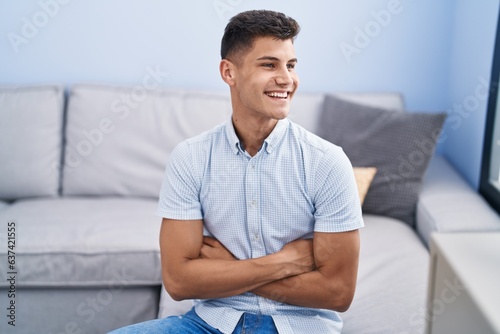 Young hispanic man smiling confident sitting with arms crossed gesture at home