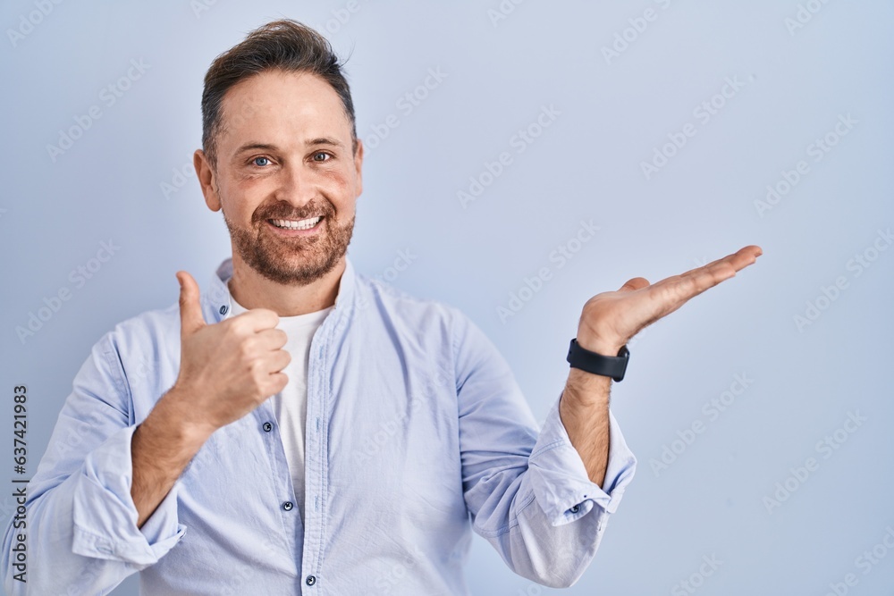 Middle age caucasian man standing over blue background showing palm hand and doing ok gesture with thumbs up, smiling happy and cheerful Middle age caucasian man standing over blue background showing palm hand and doing ok gesture with thumbs up, smiling happy and cheerful