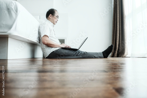 Adult man working from home. Sitting on wooden floor and using laptop in studio apartment.