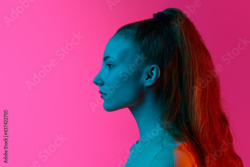 Profile view of young girl looking straight with calm emotionless face against pink studio background in neon light. Concept of human emotions, fashion, beauty, lifestyle, youth, ad
