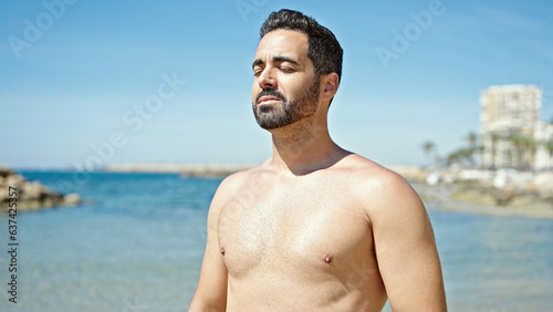 Young hispanic man tourist standing shirtless breathing at the beach