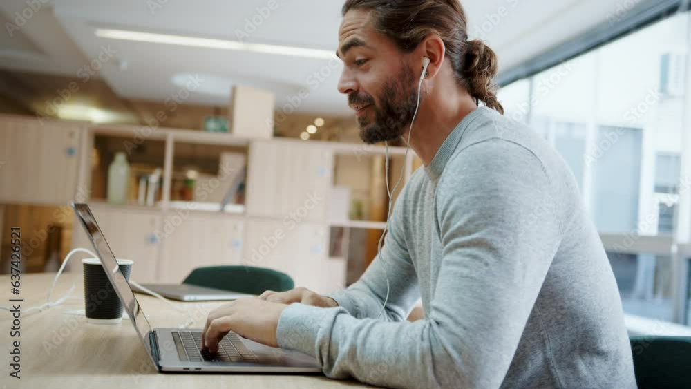 Young freelancer connecting with his colleagues using a laptop, having a discussion in a virtual meeting. Modern business man using technology to work remotely in a coworking space.