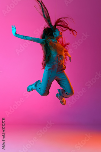 Positivity. Excited and emotional young woman cheerfully jumping against pink studio background in neon light. Concept of human emotions, fashion, beauty, lifestyle, youth, ad © master1305