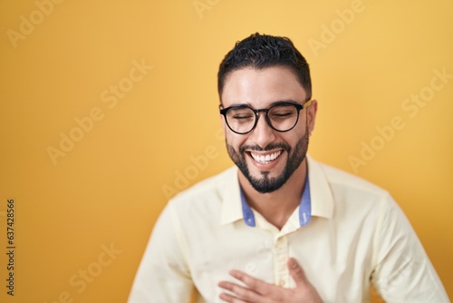 Hispanic young man wearing business clothes and glasses smiling and laughing hard out loud because funny crazy joke with hands on body.