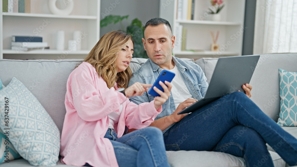 Man and woman couple using laptop and smartphone sitting on sofa at home