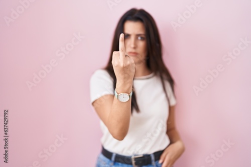 Young brunette woman standing over pink background showing middle finger  impolite and rude fuck off expression