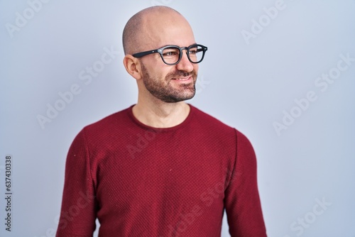 Young bald man with beard standing over white background wearing glasses looking away to side with smile on face, natural expression. laughing confident. © Krakenimages.com