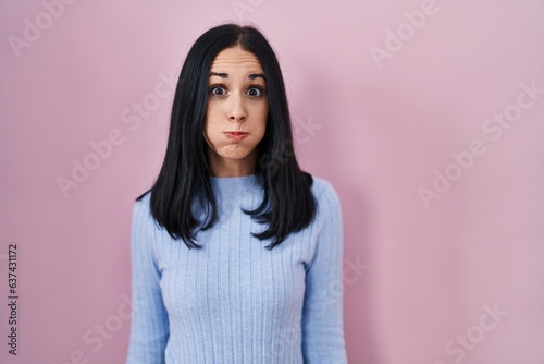 Hispanic woman standing over pink background puffing cheeks with funny face. mouth inflated with air, crazy expression. photo