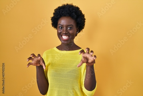 African young woman standing over yellow studio smiling funny doing claw gesture as cat, aggressive and sexy expression