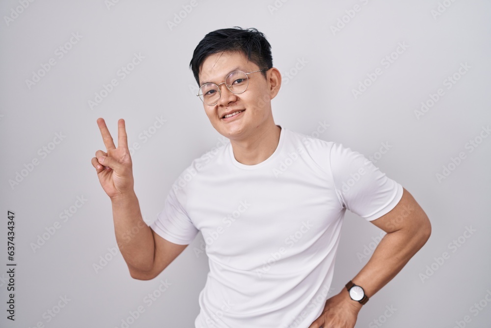 Young asian man standing over white background smiling looking to the camera showing fingers doing victory sign. number two. Young asian man standing over white background smiling looking to the camera showing fingers doing victory sign. number two.