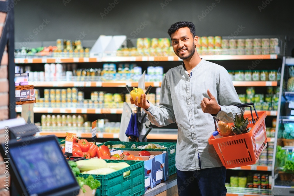 Closeup portrait, handsome young man picking up bell peppers, choosing yellow and orange vegetables in grocery store