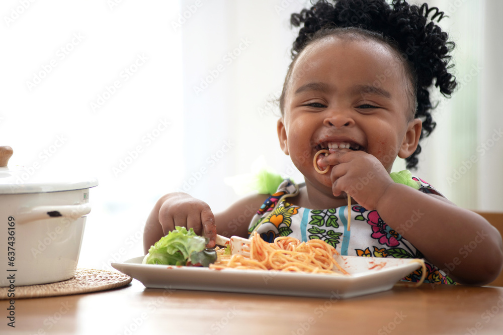 Cute African baby girl enjoys eating spaghetti with hands, eating pasta spaghetti by herself, delicious taste Cute African baby girl enjoys eating spaghetti with hands, eating pasta spaghetti by herself, delicious taste