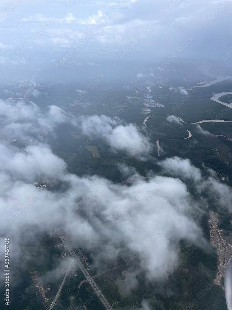 Obraz premium The image below is viewed from an airplane through the clouds. Green ground full of trees interspersed with people's houses and land.