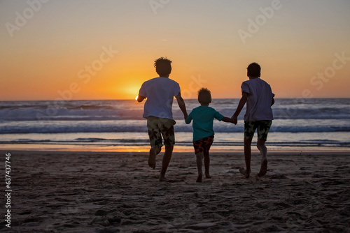 Happy children, boys, playing on the beach on sunset, kid cover in sand, smiling, laughing © Tomsickova