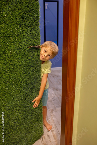 Cute blond toddler child, higing behind the door at home, peeping curiously and smiling photo