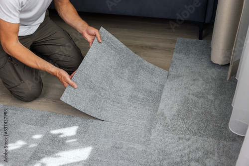 man installing self adhesive carpet tiles on floor in living room at home