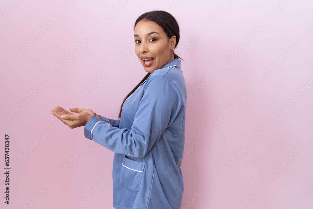 Young arab woman wearing blue pajama pointing aside with hands open palms showing copy space, presenting advertisement smiling excited happy Young arab woman wearing blue pajama pointing aside with hands open palms showing copy space, presenting advertisement smiling excited happy
