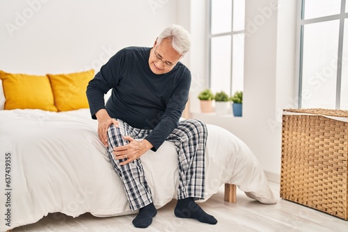 Senior man suffering for knee pain sitting on bed at bedroom