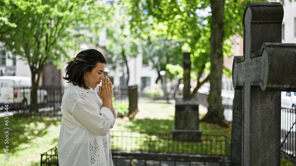 Beautiful young hispanic woman praying and mourning by tombstone at graveyard Beautiful young hispanic woman praying and mourning by tombstone at graveyard