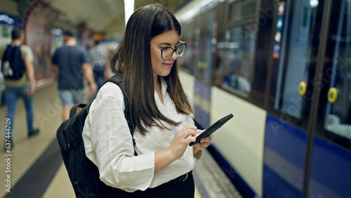 Young beautiful hispanic woman waiting for the subway using smartphone in subway station of Madrid