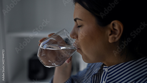 Young beautiful hispanic woman drinking a glass of water at the kitchen
