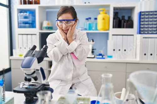 Hispanic girl with down syndrome working at scientist laboratory tired hands covering face, depression and sadness, upset and irritated for problem