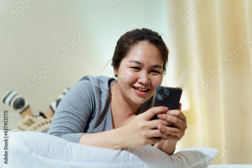 Asian oversize fat woman lying on the bed at night and chatting or messaging with a friends on smartphone before getting sleep.