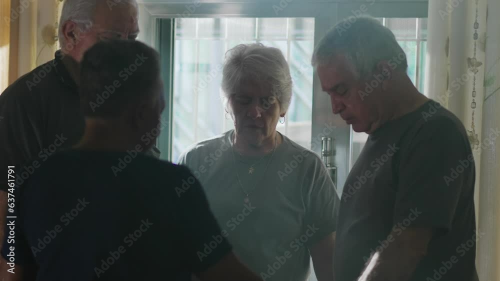 Four seniors PRAYING at home, candid group of elderly friends engaged in PRAYER and DEVOTION while standing by window with light rays shining through Four seniors PRAYING at home, candid group of elderly friends engaged in PRAYER and DEVOTION while standing by window with light rays shining through
