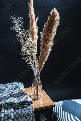 interior and home decor concept - blanket and dry plants in vase on bench and pillows on floor in dark room