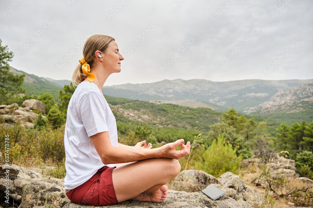 Woman with smartphone sitting in lotus pose on rock