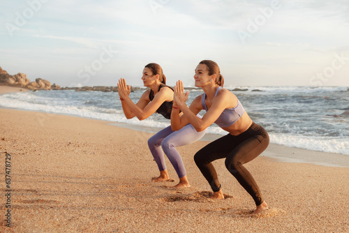 Positive pretty young caucasian women enjoy workout, fitness, pilates together, squats on sea beach