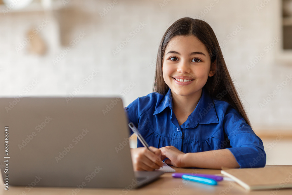 Teenage school girl posing at desk with laptop writing indoors Teenage school girl posing at desk with laptop writing indoors
