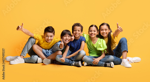 Foto Happy multiethnic kids sitting on floor, showing thumb ups