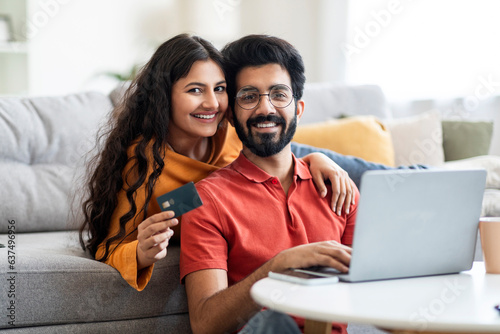 Internet Purchases. Portrait Of Smiling Indian Couple With Laptop And Credit Card