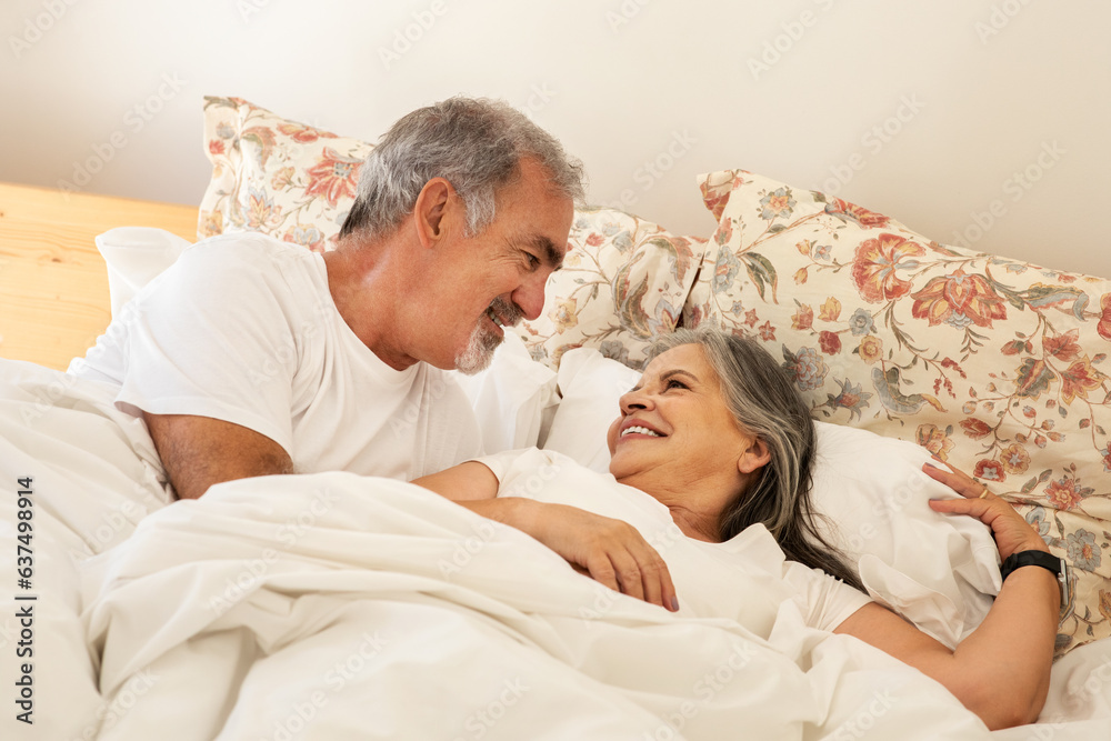 Smiling happy old caucasian husband wakes up wife in bed, enjoy good morning together in bedroom Smiling happy old caucasian husband wakes up wife in bed, enjoy good morning together in bedroom