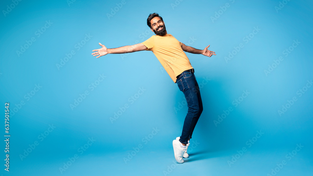 Positive funny middle aged indian man fooling on blue studio background, standing on toes, full length, panorama Positive funny middle aged indian man fooling on blue studio background, standing on toes, full length, panorama