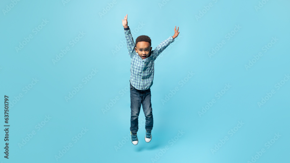 Playful african american little boy jumping with hands up, blue background, full length, panorama, free space Playful african american little boy jumping with hands up, blue background, full length, panorama, free space